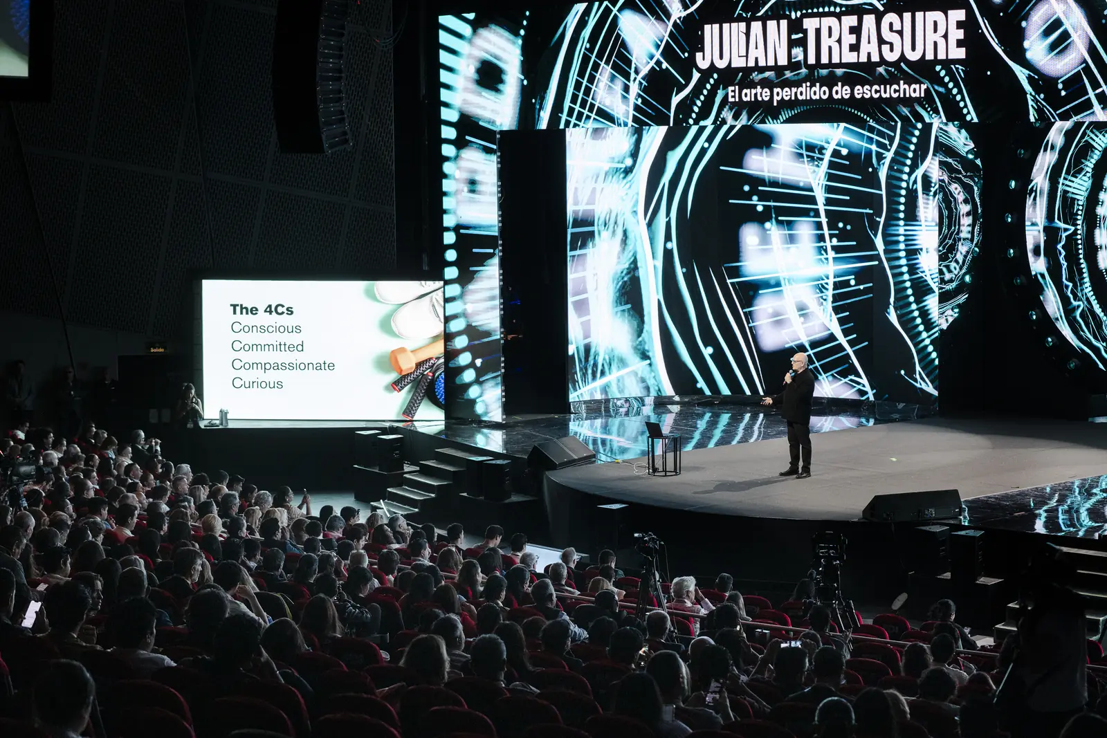 Julian Treasure on stage before a packed auditorium, a slide beside him